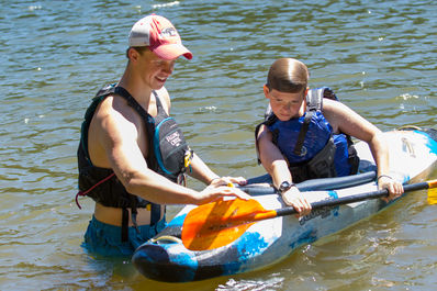 Counselor teaching a camper how to roll a kayak on our camp lake.