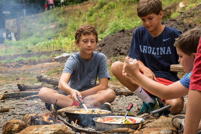 Campers learning how to cook on a campfire.